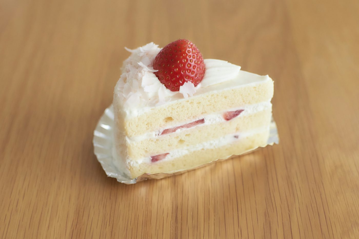 A slice of layered sponge cake with cream, strawberries and coconut flakes