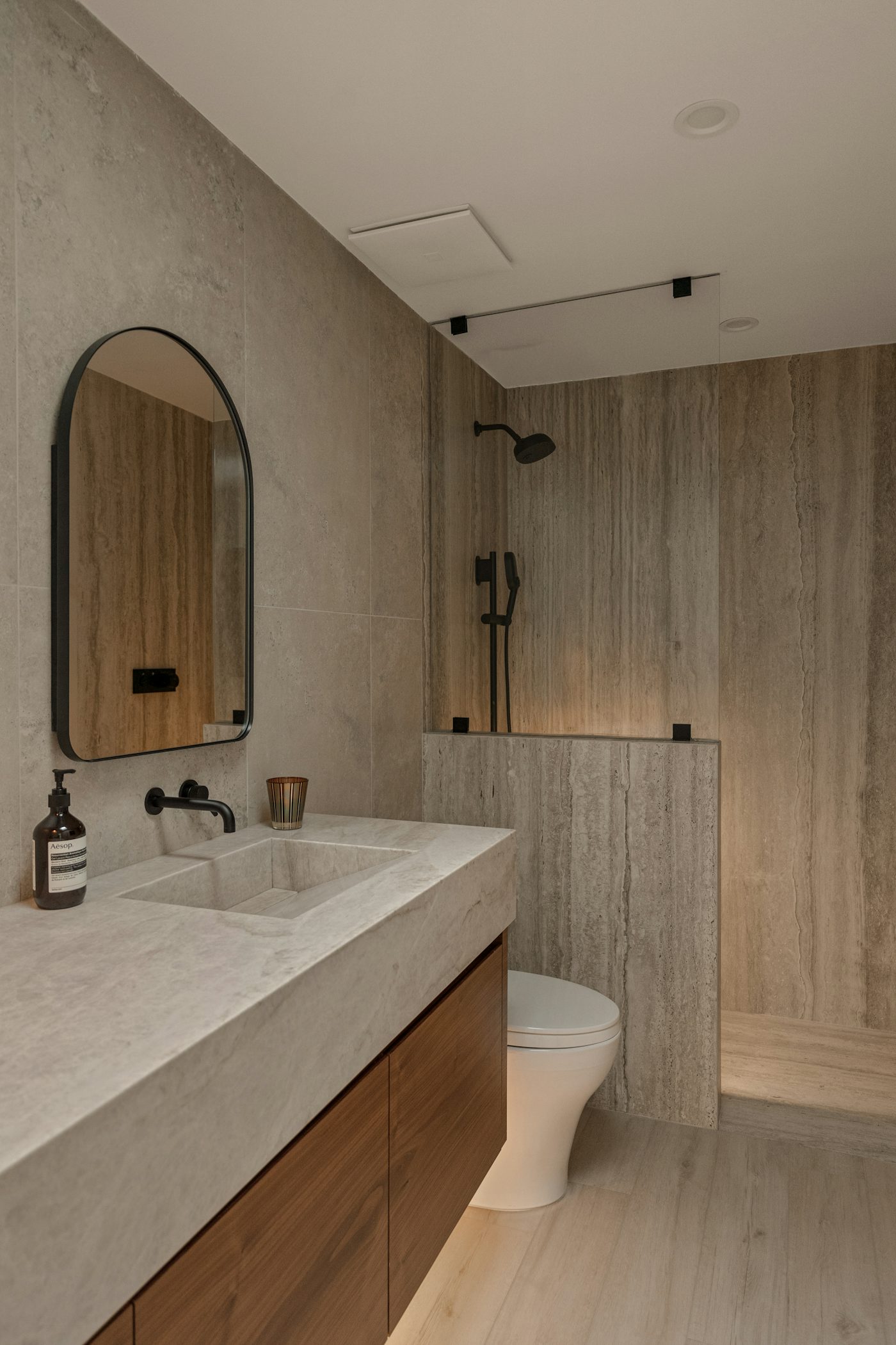 A finished shower room with stone tiles, a walnut vanity and a glass shower screen