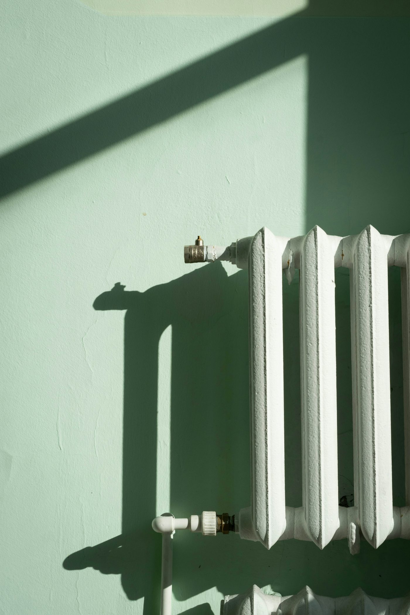 A white cast-iron radiator on a pale green wall in low sunlight